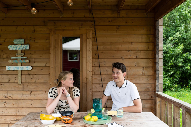 Zwei Personen sitzen an einem Holztisch vor dem Safari-Zelt Boerderij huisje im Beloofde Land, Niederlande.
