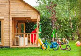 Safari tent Jungle huisje at Beloofde Land in the Netherlands with bikes, toys, and children playing on the grass.