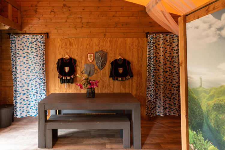 Interior of Ridder & Prinsessen house in a safari tent with knight costumes and shields on wooden walls.