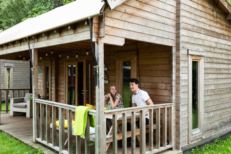 Zwei Personen unterhalten sich auf der Veranda eines Holzhauses im Ridder & Prinsessen huisje, Beloofde Land, Niederlande.