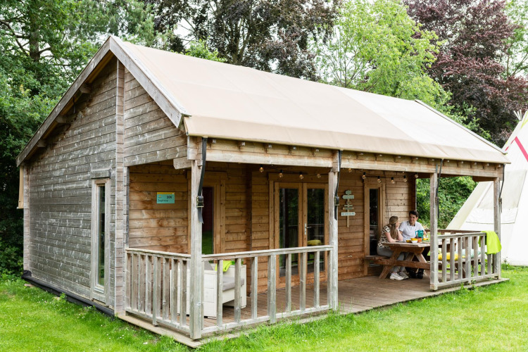 Tenda safari chiamata Ridder & Prinsessen huisje con veranda in legno immersa nel verde e due persone fuori.