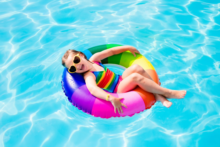 Child in rainbow swim ring and swimsuit relaxing in pool at Beloofde Land, Netherlands.