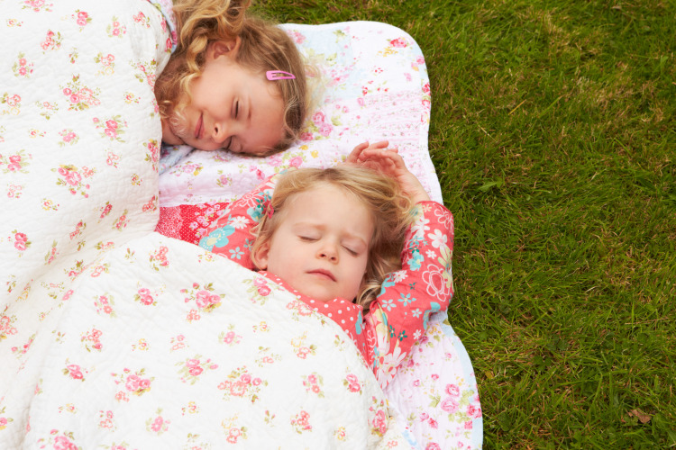 Due bambini dormono serenamente su una coperta floreale vicino alla tenda safari a Beloofde Land, Paesi Bassi.