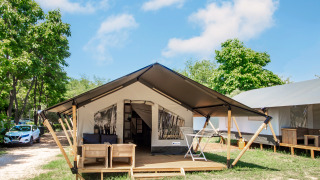 Glampingverblijf met moderne tent, houten terras, buitensalon en omgeven door groene natuur.