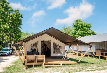 Glampingverblijf met moderne tent, houten terras, buitensalon en omgeven door groene natuur.