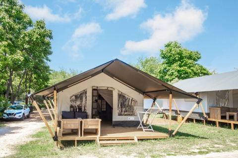 Alloggio glamping con tenda moderna, veranda in legno, area salotto esterna e tanto verde intorno.