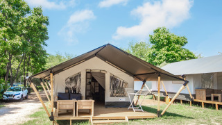 Alloggio glamping con tenda moderna, veranda in legno, area salotto esterna e tanto verde intorno.