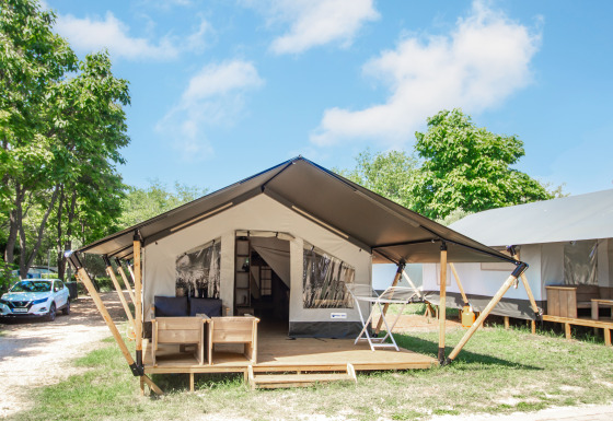 Glamping accommodation featuring a modern tent, wooden deck, outdoor seating, and lush greenery.