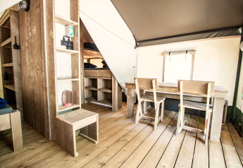 Moderne glamping-indkvartering med træmøbler, spisebord, stole, køjesenge og lyst trægulv.