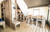 Alloggio glamping moderno con mobili in legno, tavolo da pranzo, sedie, letti a castello e pavimento in legno.