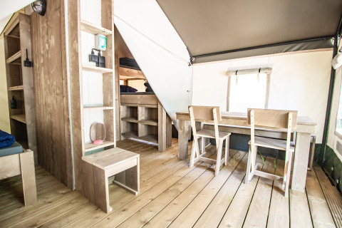 Moderne glampingaccommodatie met houten meubels, eettafel, stoelen, stapelbedden en houten vloer.