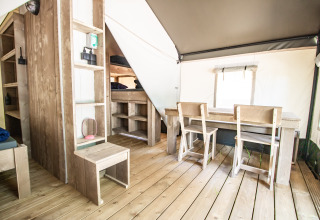 Moderne glampingaccommodatie met houten meubels, eettafel, stoelen, stapelbedden en houten vloer.