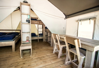 Binnenzicht van een glamping-tent met houten vloer, simpele bedden en eettafel met stoelen.
