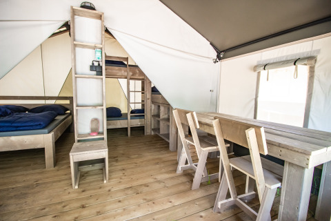 Interior de una tienda de glamping con piso de madera, camas sencillas y mesa de comedor con sillas.