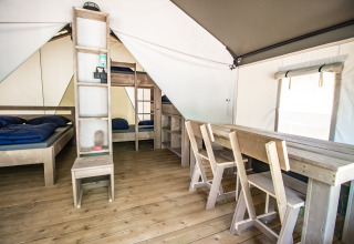 Interno di una tenda glamping con pavimento in legno, letti semplici e tavolo da pranzo con sedie.