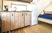 Interior de una tienda glamping con suelo de madera, cocina, nevera blanca y cama con mantas azules.