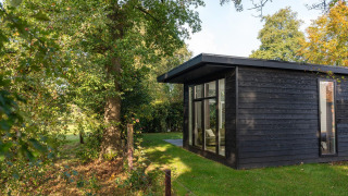 Black wooden nature cabin at Holiday Park Mölke, Netherlands, set amidst lush green trees and grass.