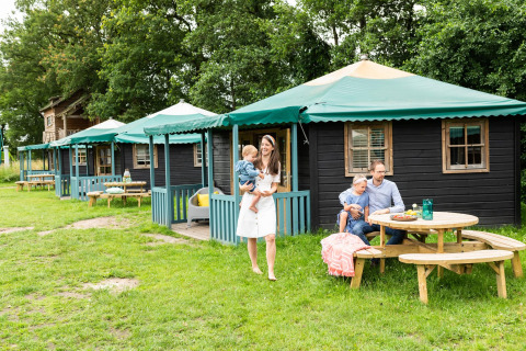 Familia disfruta al aire libre frente a una casa de naturaleza llamada Forest cottage con bancos de madera.