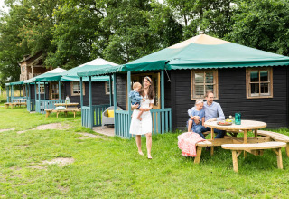 Gezin ontspant buiten aan een Forest cottage natuurhuisje met groene daken en houten picknicktafels.