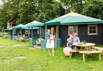 Familia disfruta al aire libre frente a una casa de naturaleza llamada Forest cottage con bancos de madera.