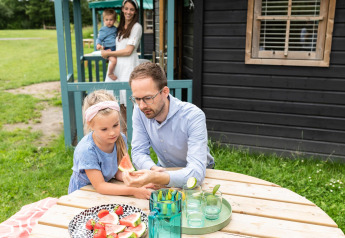 Famiglia gusta anguria e fragole davanti a un cottage nella natura a Beloofde Land, Paesi Bassi.