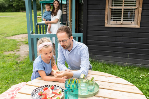 Familie isst Wassermelone und Erdbeeren am Tisch vor Waldhaus auf dem Beloofde Land, Niederlande.
