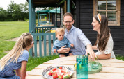 Famiglia che gusta frutta a un tavolo esterno vicino al cottage nel bosco a Beloofde Land, Olanda.