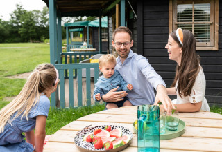 Familie genießt draußen Obst am Tisch vor einer Waldhütte im Beloofde Land, Niederlande.
