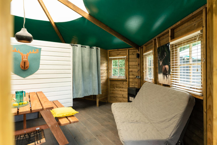 Interior of a cozy wooden forest cottage with green ceiling, sofa bed, and picnic table at Beloofde Land, Netherlands.