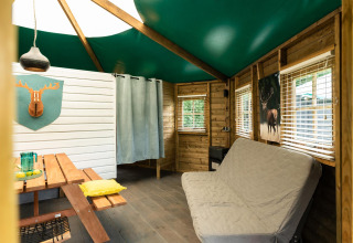 Innenraum einer gemütlichen Waldhütte mit grüner Decke, Schlafsofa und Picknicktisch in den Niederlanden.