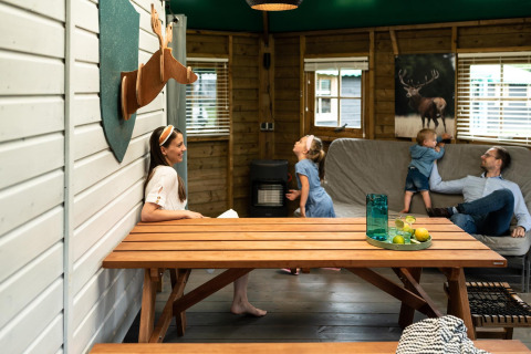 Familie hygger sig indendørs i skovhytte på Beloofde Land, Nederlandene, med træmøbler og dekorationer.