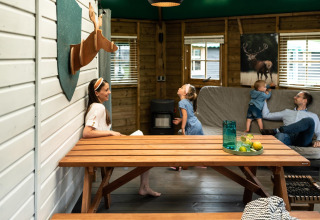 Familie entspannt sich in einer Waldhütte auf dem Beloofde Land, Niederlande, mit Holzmöbeln und Dekor.