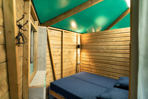 Vue intérieure du Forest cottage au Beloofde Land, Pays-Bas, avec des murs en bois et un lit double.