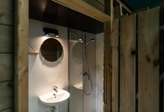 Modernes Badezimmer mit Waschbecken, Dusche und Spiegel in einer Waldhütte im Beloofde Land, Niederlande.