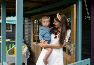 Madre sostiene a su hijo en la entrada de una casa natural Forest cottage en Beloofde Land, Países Bajos.