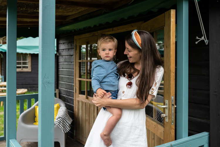 Mother holding her child at the entrance of a forest cottage nature house at Beloofde Land in the Netherlands.