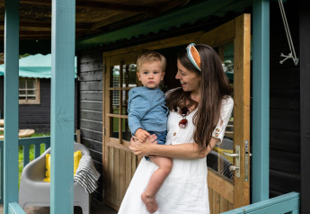 Madre sostiene a su hijo en la entrada de una casa natural Forest cottage en Beloofde Land, Países Bajos.