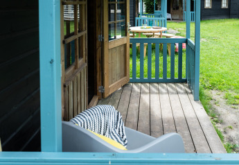 Veranda della Forest cottage al Beloofde Land, Paesi Bassi, con porta aperta e prato verde all’esterno.