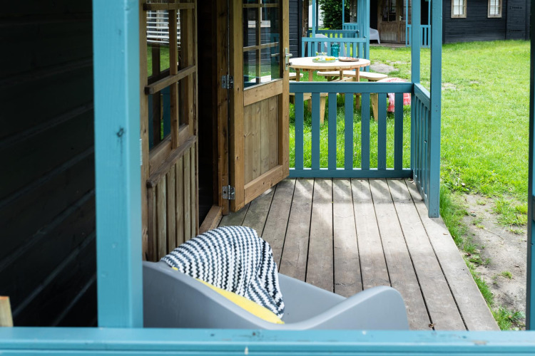 Cozy porch at Forest cottage, Beloofde Land, Netherlands, with open door, blue railing, and grassy yard.