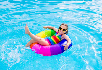 Niña con bañador de arcoíris y gafas de sol en flotador colorido en piscina de Forest cottage, Beloofde Land.