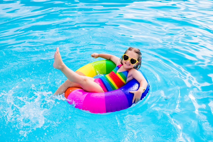 Child in rainbow swimsuit and heart sunglasses floating on colorful ring in pool at Forest cottage, Beloofde Land.