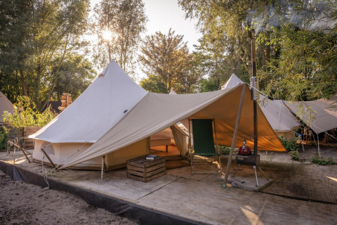 Tienda de campaña Solo Tipi en RØSTIG, Países Bajos, sobre plataforma de madera con árboles al fondo.