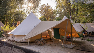 Tienda de campaña Solo Tipi en RØSTIG, Países Bajos, sobre plataforma de madera con árboles al fondo.