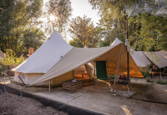 Tienda de campaña Solo Tipi en RØSTIG, Países Bajos, sobre plataforma de madera con árboles al fondo.