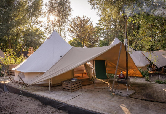 Tienda de campaña Solo Tipi en RØSTIG, Países Bajos, sobre plataforma de madera con árboles al fondo.