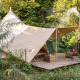 Telt i tipi-stil med et overdækket trædæk midt i frodig natur, omgivet af grønne træer og buske.