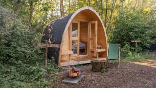 Una Solo Pod en RØSTIG, Países Bajos, rodeada de bosque, con fogata, silla y tocón al frente.