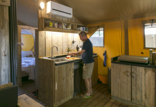 Hombre cocinando en la cocina rústica de la SunLodge Bintulu en Camping Village Poljana, Croacia.