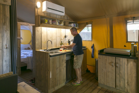 Hombre cocinando en la cocina rústica de la SunLodge Bintulu en Camping Village Poljana, Croacia.