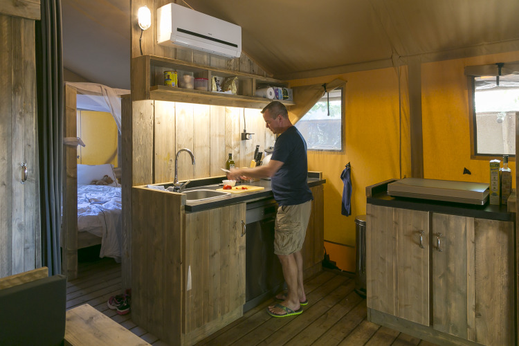 Hombre cocinando en la cocina rústica de la SunLodge Bintulu en Camping Village Poljana, Croacia.
